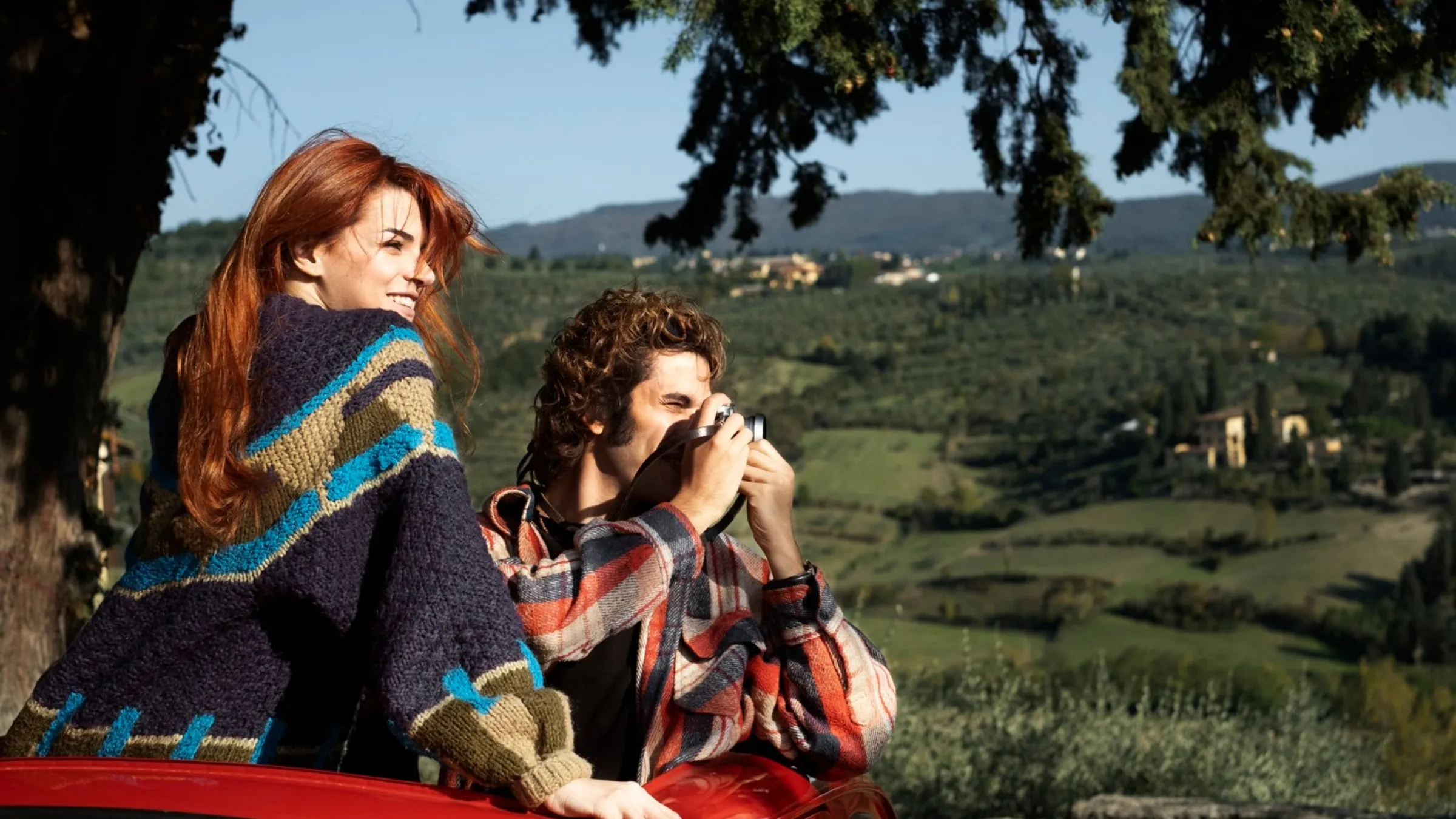 Due viaggiatori guardano le colline coltivate a ulivi; lui scatta una foto al paesaggio