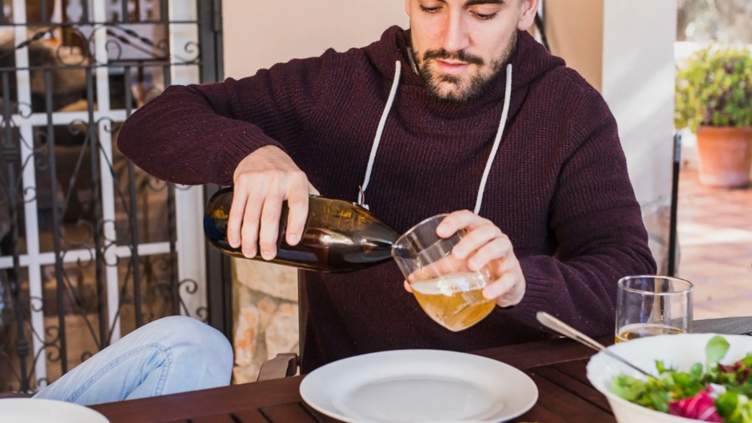 Un ragazzo versa da bere a una tavola apparecchiata all’aperto, con pizza, patatine e insalata